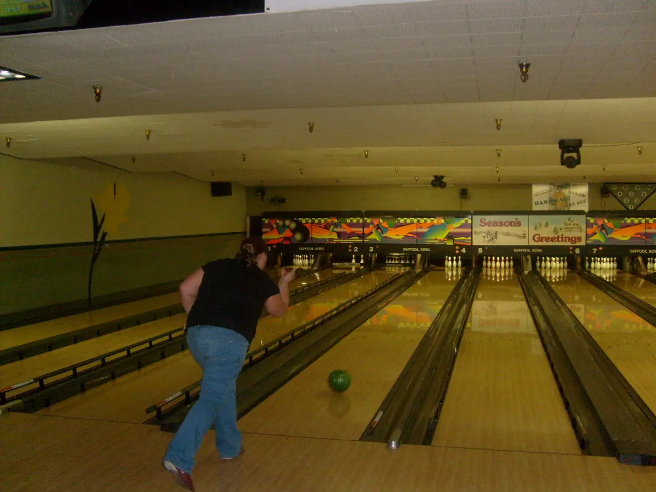 In this image we can see a person doing bowling. In addition to this we can see electric lights and...