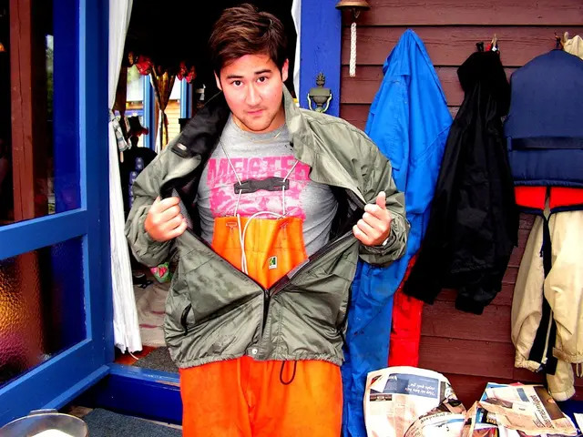In this image, in the middle there is a jacket, t shirt. In the background there are jackets,...